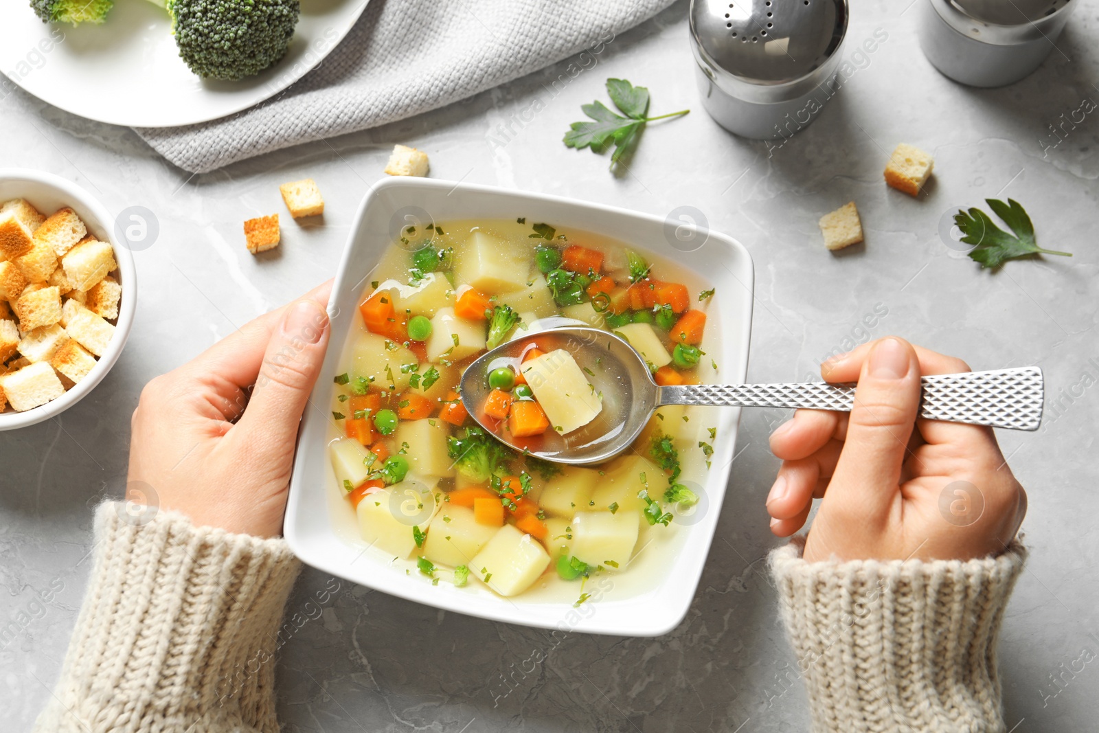 Photo of Woman eating fresh homemade vegetable soup at grey marble table, top view