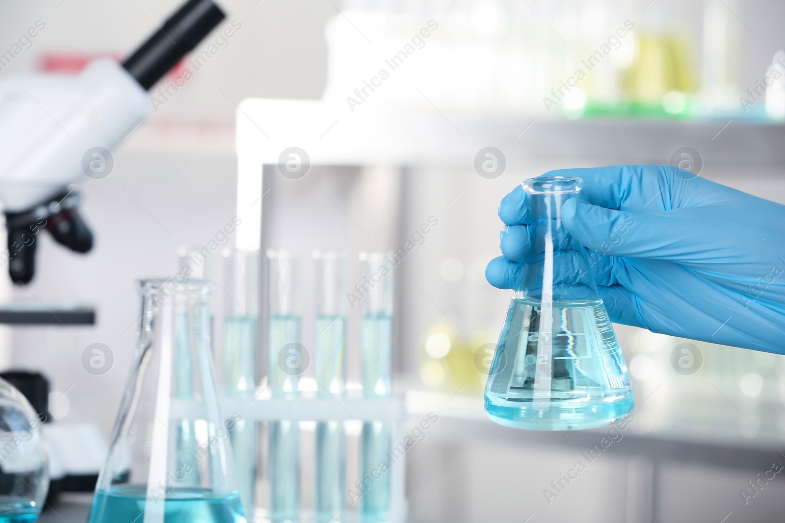 Photo of Analyst holding flask with fluid in laboratory, closeup. Chemical analysis