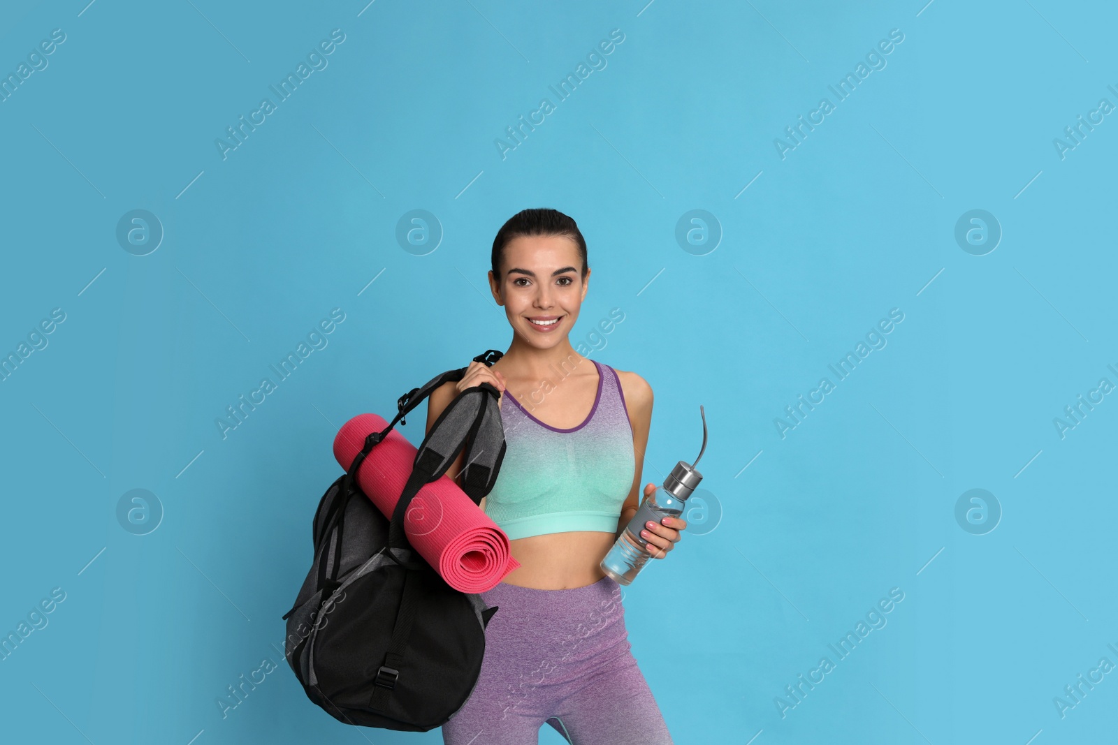 Photo of Beautiful woman with sports bag and bottle of water on light blue background