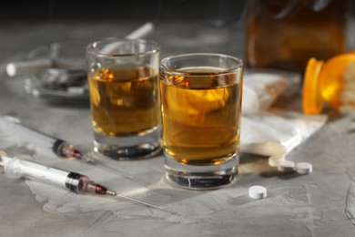Photo of Alcohol and drug addiction. Whiskey in glasses, syringes, pills and cocaine on grey table, closeup