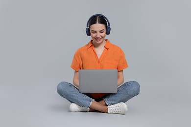 Happy woman in headphones using laptop on light gray background