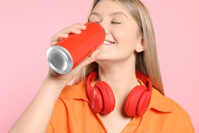 Beautiful happy woman drinking from red beverage can on pink background, closeup