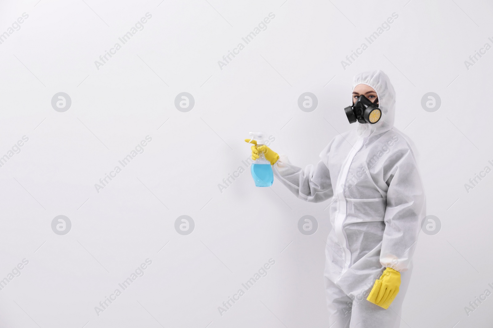 Photo of Woman in protective suit cleaning mold with sprayer on wall. Space for text