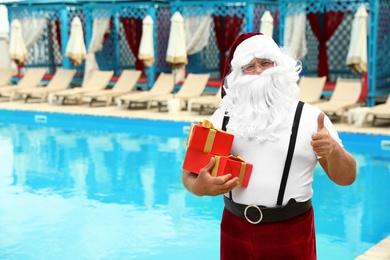 Photo of Authentic Santa Claus with gift boxes near pool at resort