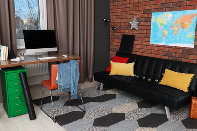 Photo of Stylish teenager's room with computer, black sofa and world map on brick wall