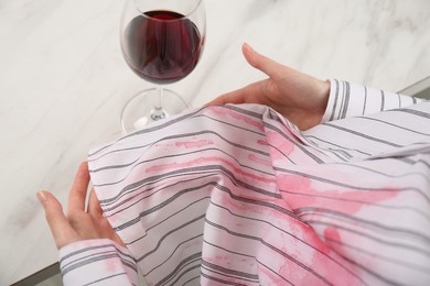 Woman with spilled wine over her shirt near glass at marble table, above view