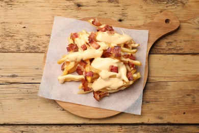 Photo of Delicious French fries with bacon and cheese sauce on wooden table, top view