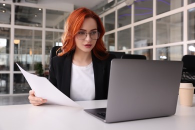 Photo of Woman with papers working on laptop at white desk in office