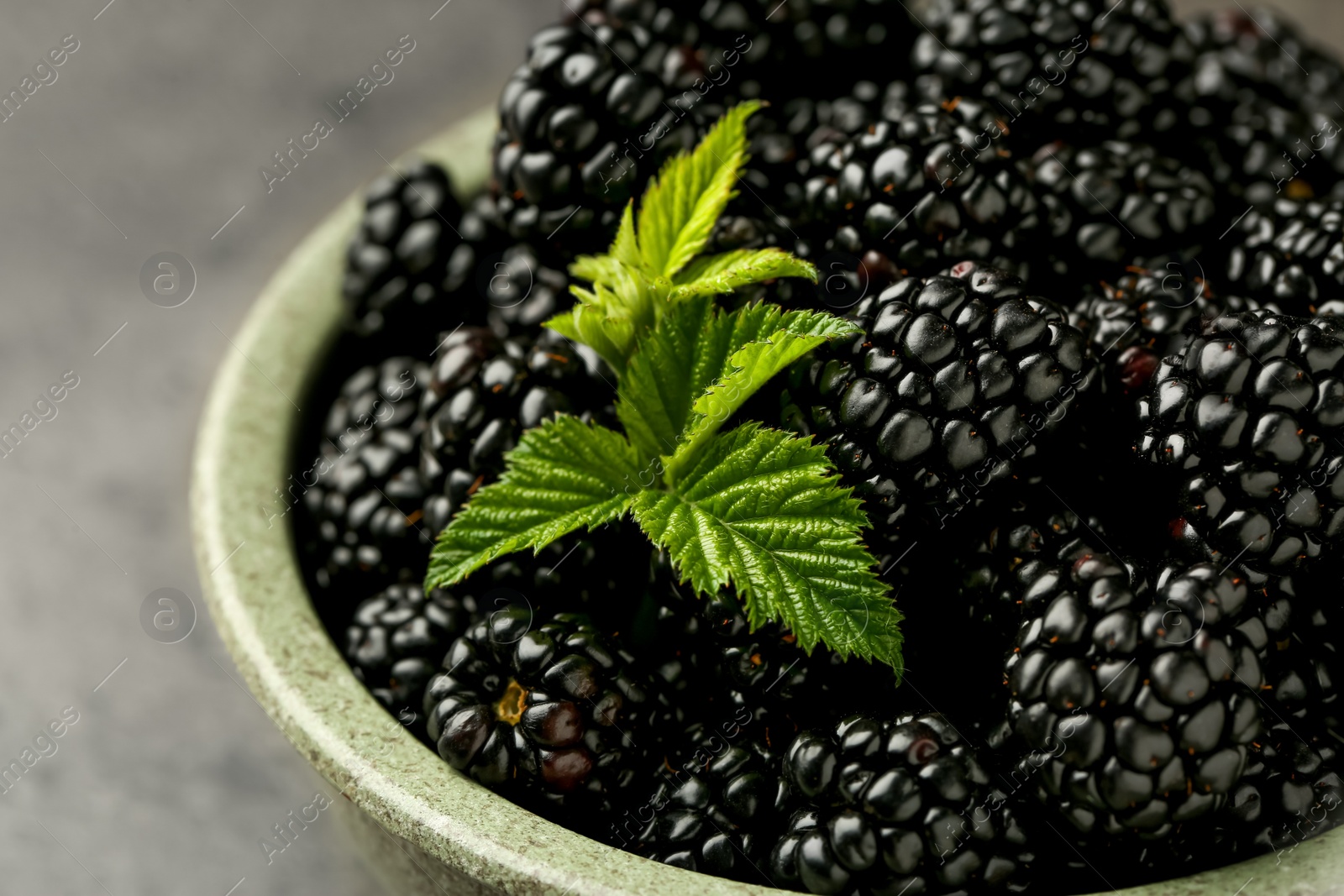 Photo of Bowl with fresh ripe blackberries on grey table, closeup