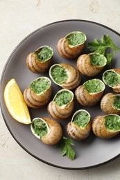 Photo of Delicious cooked snails with parsley and lemon on light table, top view