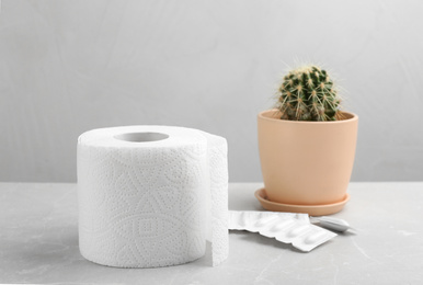 Photo of Roll of toilet paper, suppositories and cactus on table. Hemorrhoid problems