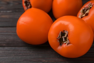 Photo of Delicious ripe persimmons on dark wooden table, closeup