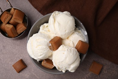 Scoops of ice cream with caramel candies in bowl on textured table, flat lay