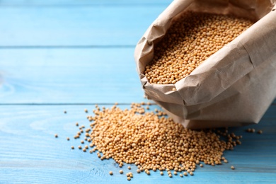 Mustard seeds in paper bag on turquoise wooden table. Space for text