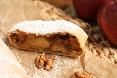Photo of Piece of delicious apple strudel with walnuts and powdered sugar on parchment paper, closeup