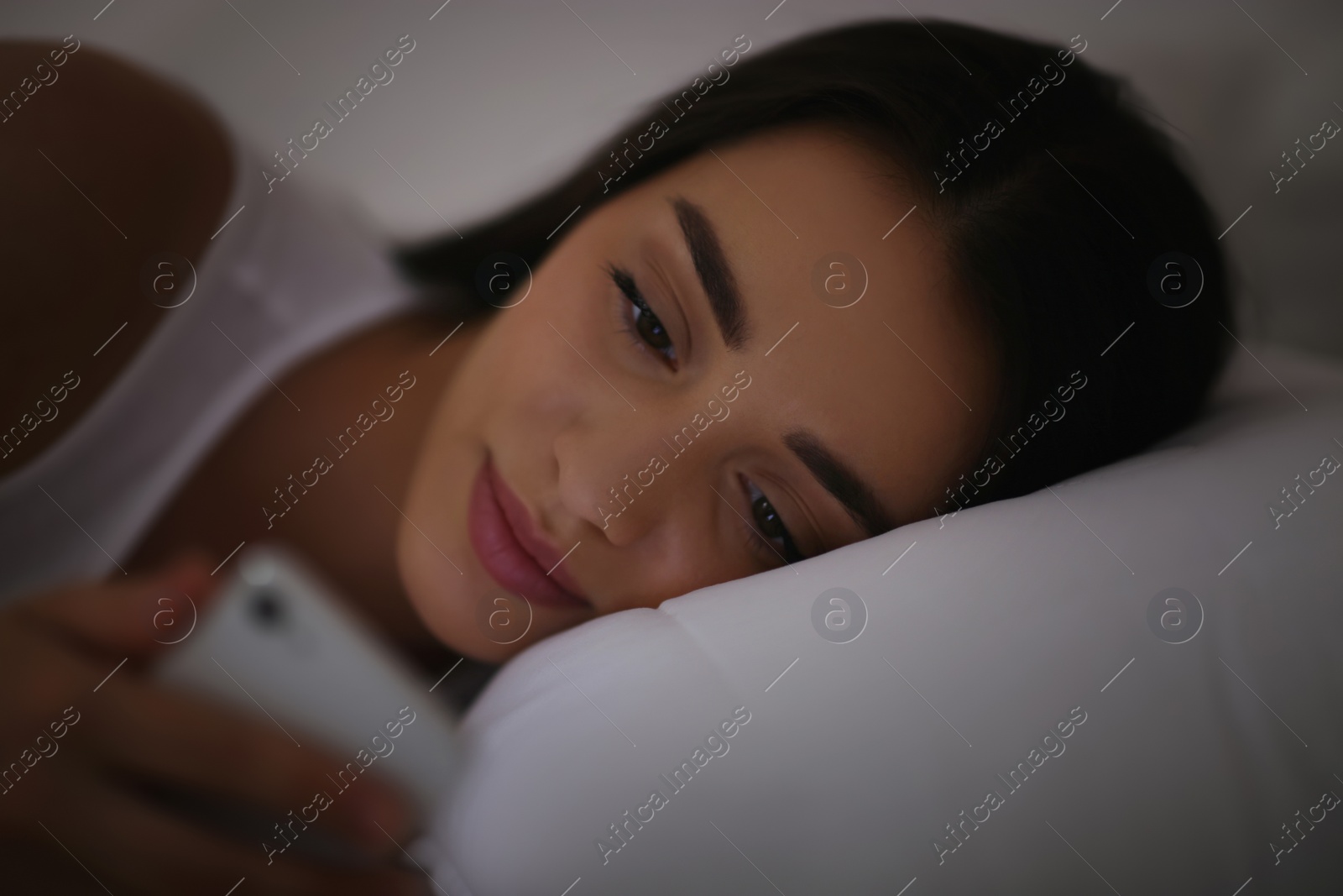 Photo of Young woman with nomophobia using smartphone in bed at night. Insomnia concept