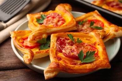 Photo of Fresh delicious puff pastry with cheese, tomatoes and parsley on wooden table, closeup