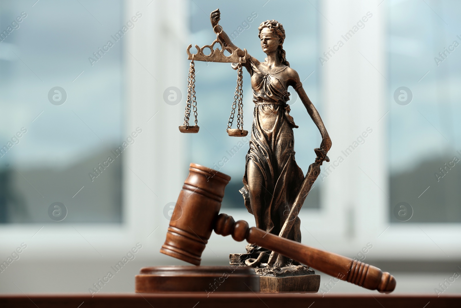 Photo of Figure of Lady Justice, gavel on table indoors, closeup. Symbol of fair treatment under law