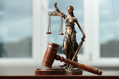 Figure of Lady Justice, gavel on table indoors, closeup. Symbol of fair treatment under law