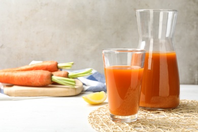 Photo of Glass and carafe with fresh carrot juice on white wooden table, space for text