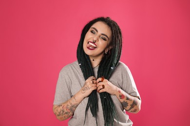 Photo of Beautiful young woman with tattoos on arms, nose piercing and dreadlocks against pink background