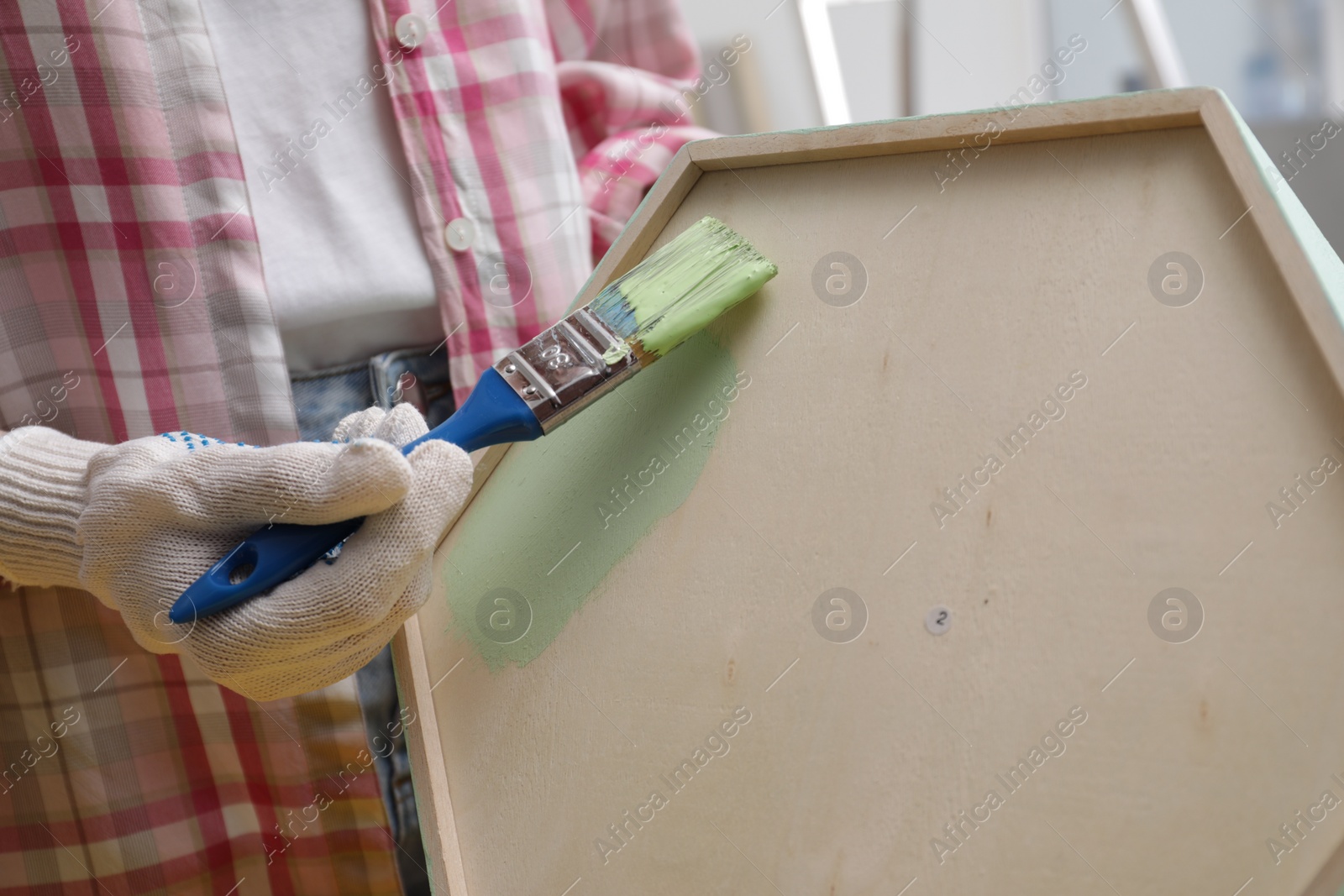 Photo of Woman painting honeycomb shaped shelf with brush indoors, closeup