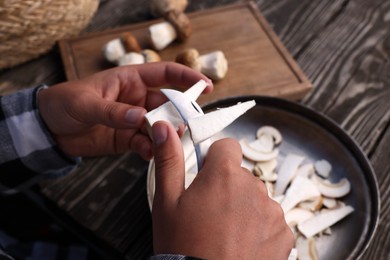 Photo of Man slicing mushrooms at wooden table, closeup