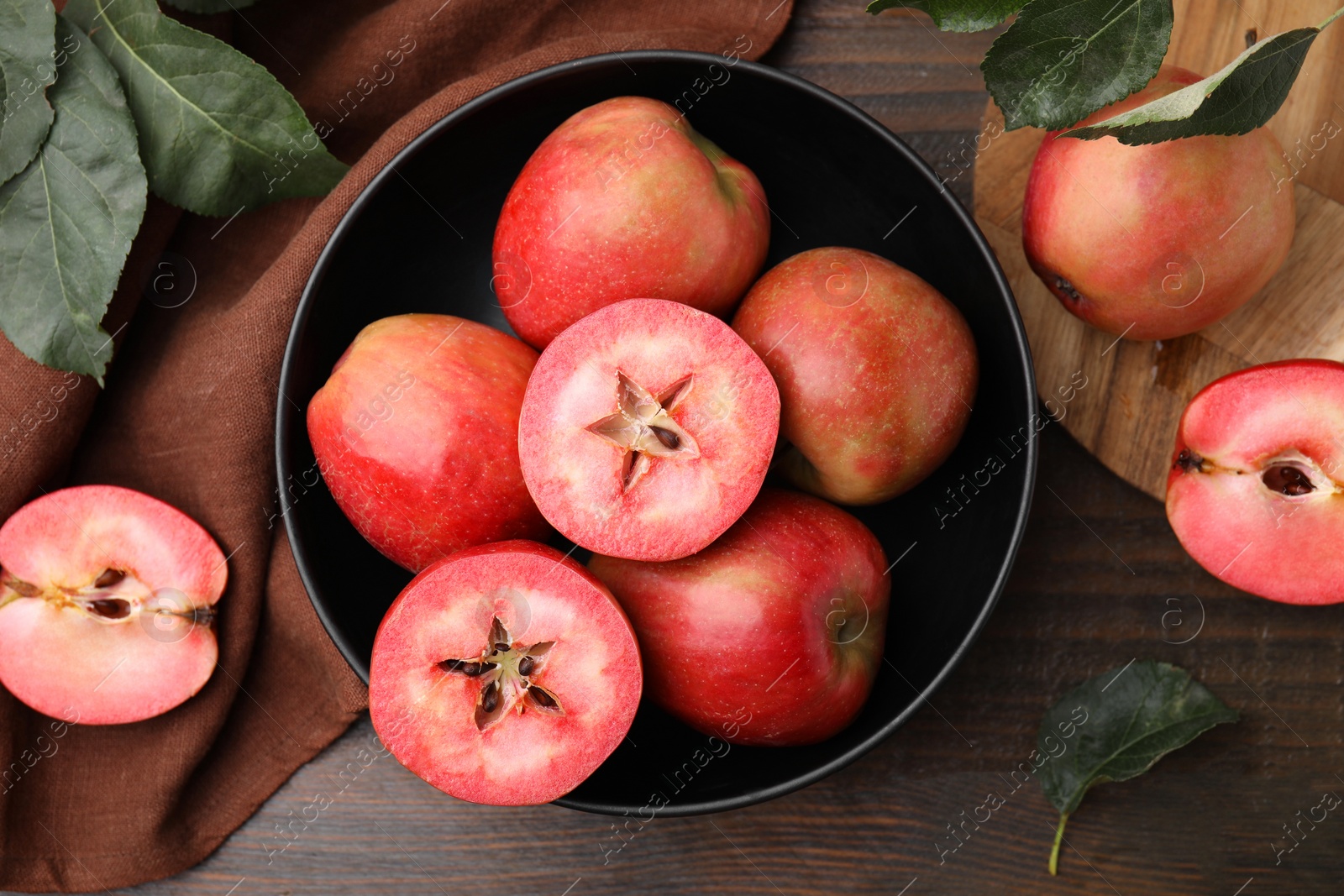 Photo of Tasty apples with red pulp and leaves on wooden table, flat lay
