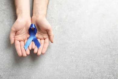 Man holding blue ribbon on grey background, top view. Cancer awareness