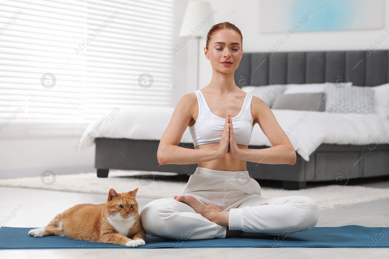 Photo of Beautiful woman with cute red cat practicing yoga on mat at home