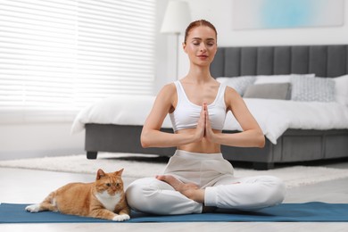 Beautiful woman with cute red cat practicing yoga on mat at home