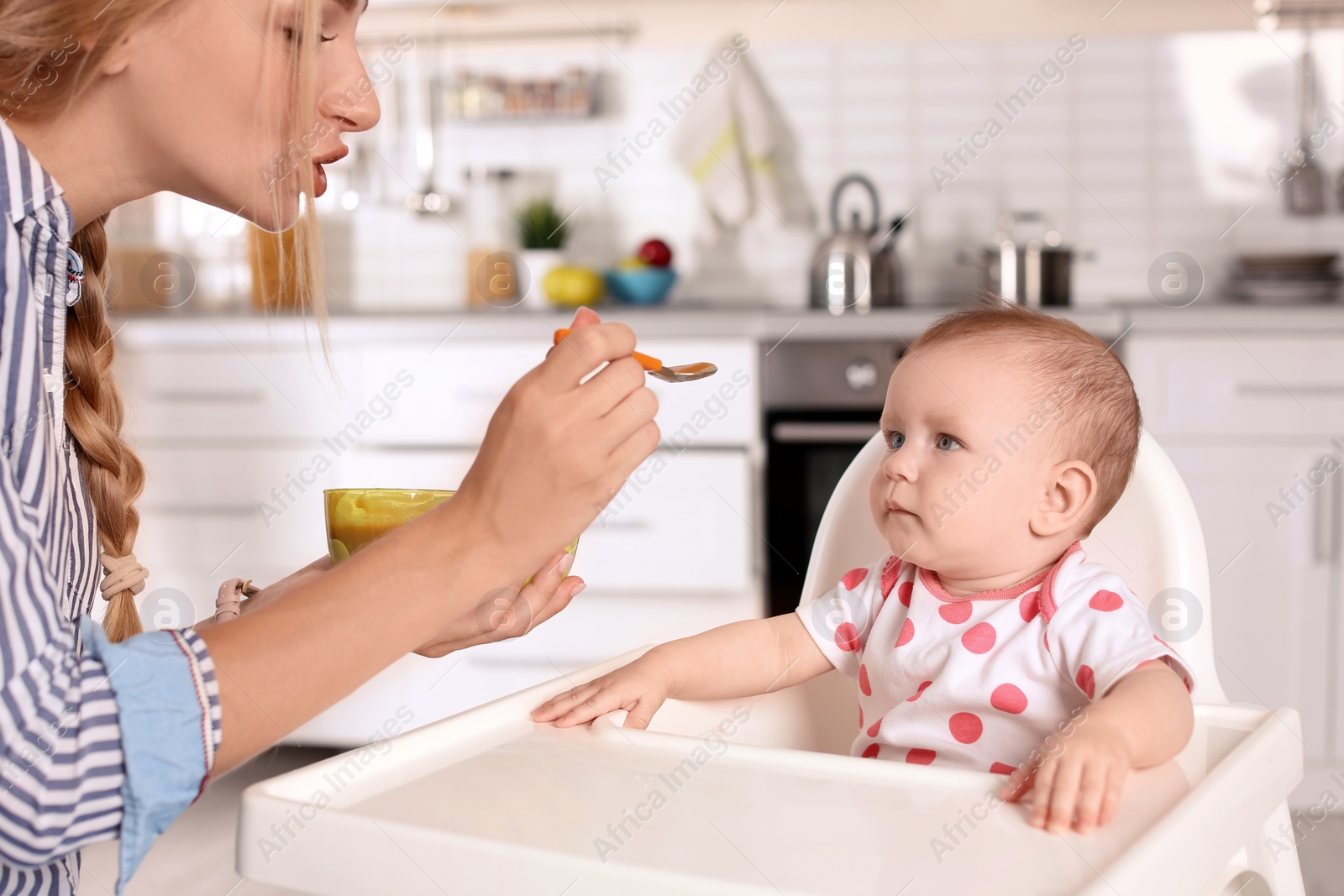 Photo of Woman feeding her child in highchair indoors. Healthy baby food