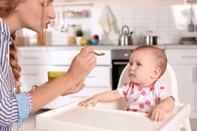 Woman feeding her child in highchair indoors. Healthy baby food