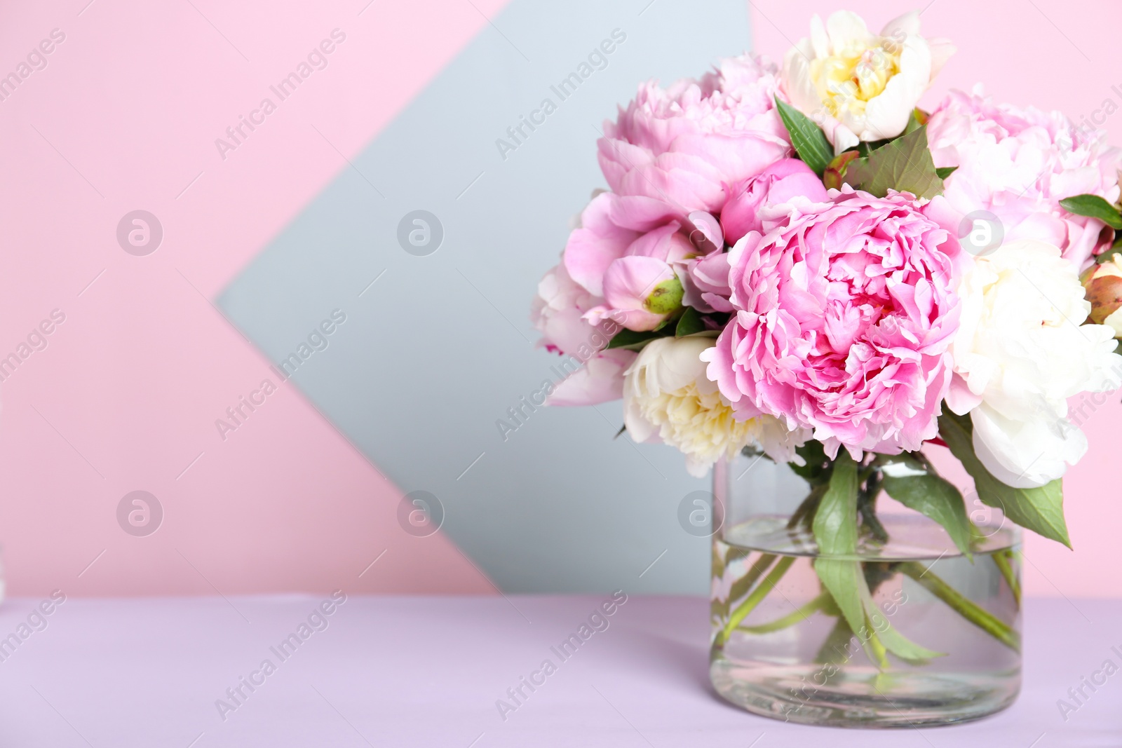Photo of Bouquet of beautiful peonies in vase on lilac table. Space for text