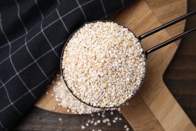 Photo of Raw barley groats in scoop on wooden table, top view