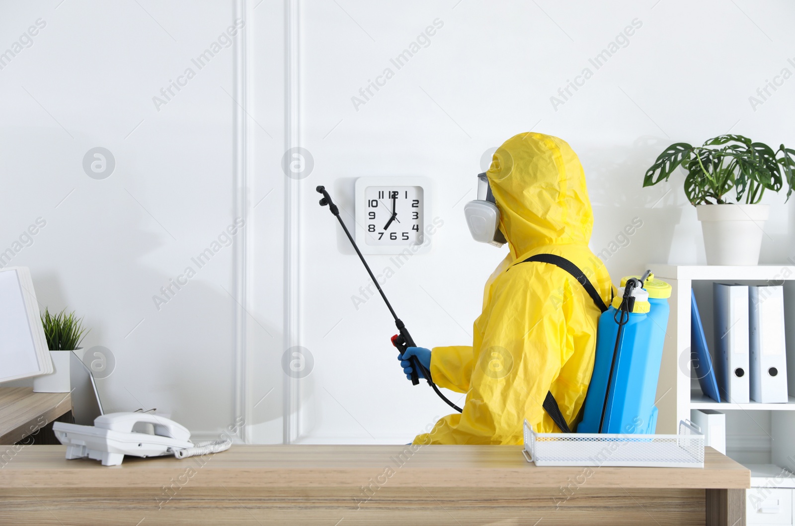 Photo of Employee in protective suit sanitizing office. Medical disinfection