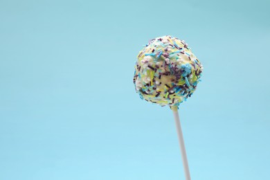 Photo of Delicious confectionery. Sweet cake pop decorated with sprinkles on light blue background, closeup. Space for text.