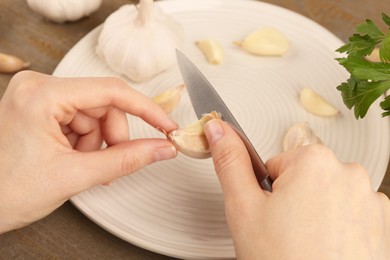 Woman peeling fresh garlic at table, closeup