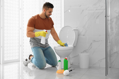 Photo of Young man cleaning toilet bowl in bathroom