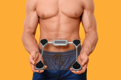 Photo of Athletic man holding scales on orange background, closeup. Weight loss concept