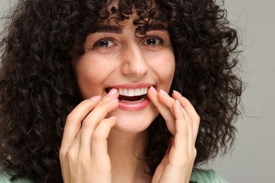 Young woman applying whitening strip on her teeth against grey background