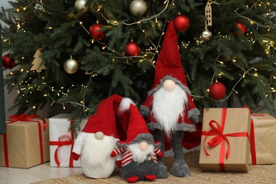 Photo of Funny decorative gnomes and gift boxes under Christmas tree indoors