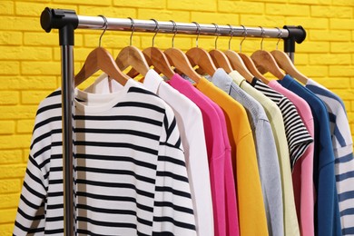 Rack with different stylish clothes near yellow brick wall