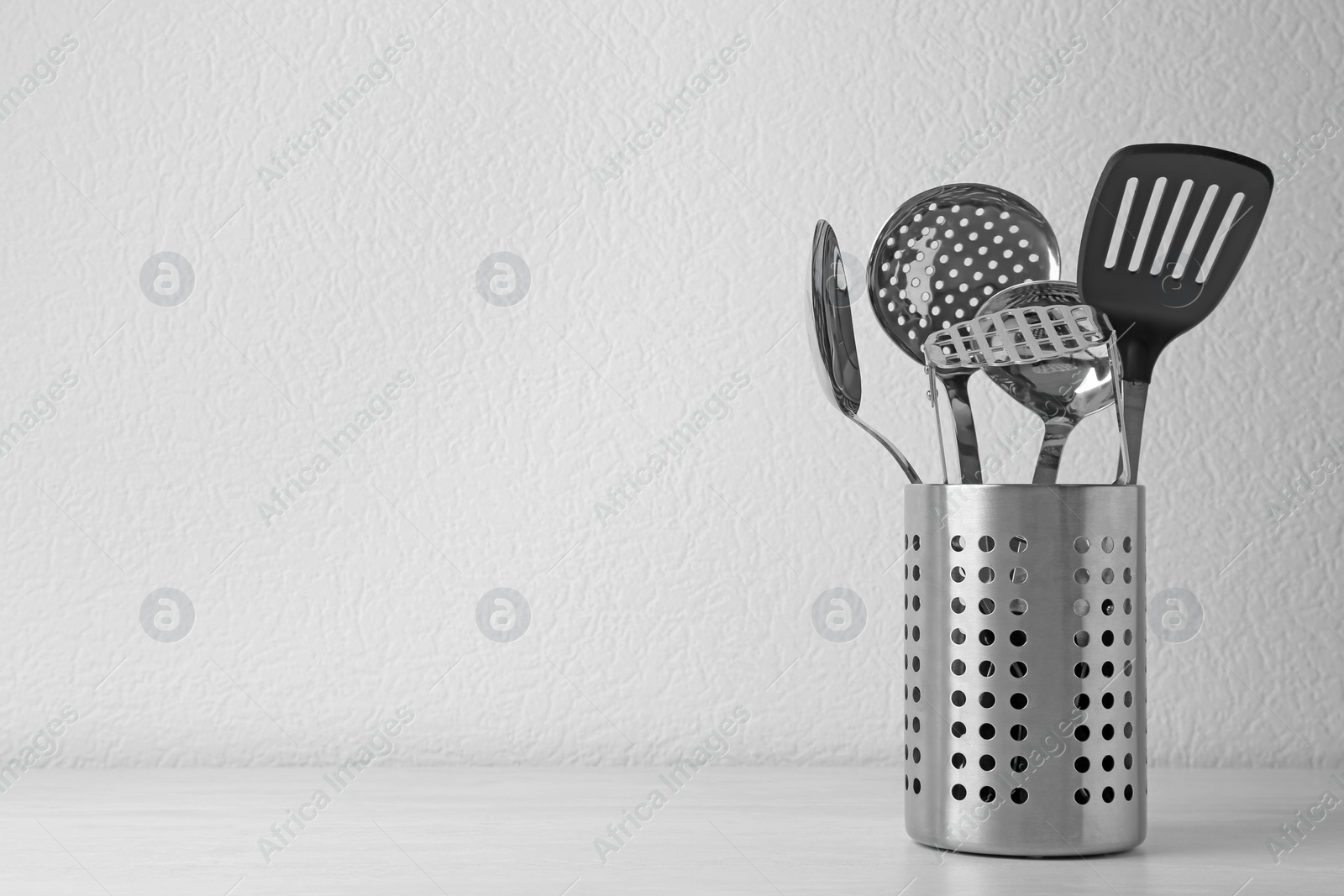 Photo of Set of kitchen utensils in stand on wooden table near light wall. Space for text