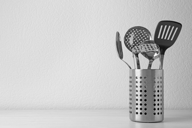 Photo of Set of kitchen utensils in stand on wooden table near light wall. Space for text