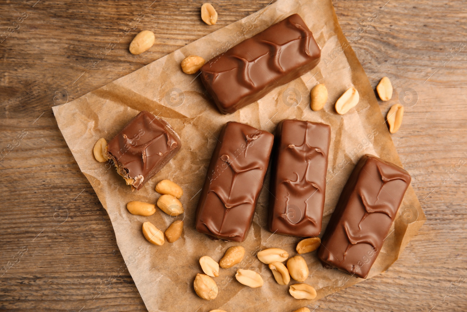 Photo of Chocolate bars with nuts and parchment on wooden table, flat lay