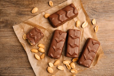 Photo of Chocolate bars with nuts and parchment on wooden table, flat lay