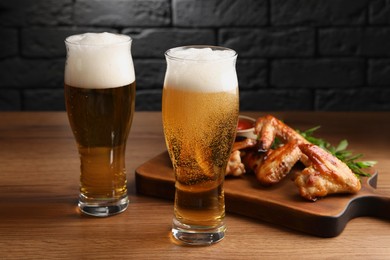 Glasses with beer and delicious baked chicken wings on wooden table