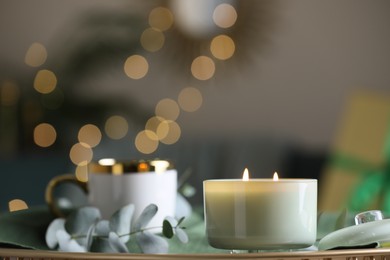 Beautiful burning candle, cup and eucalyptus branch on table indoors. Bokeh effect