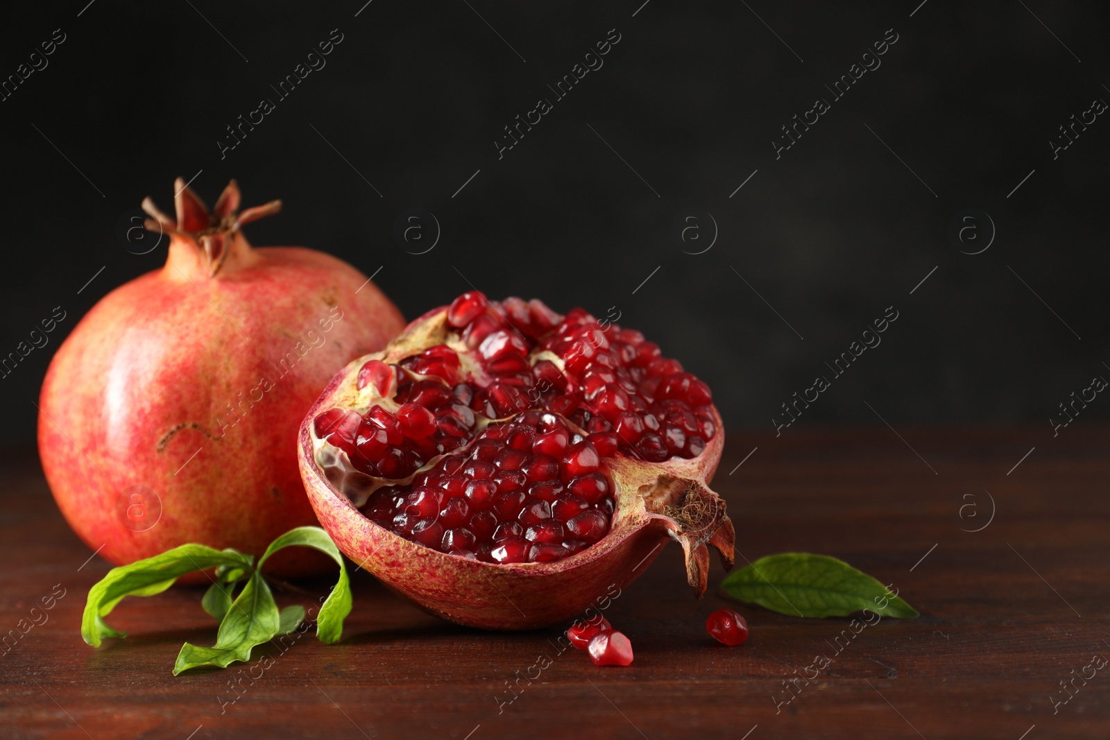 Photo of Fresh pomegranates and green leaves on wooden table, space for text